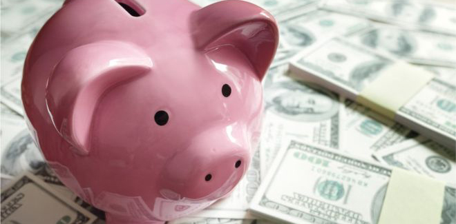 Piggy Bank sitting on a pile of hundred dollar bills