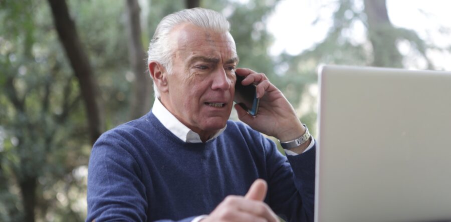 Old man on Phone looking frustrated while looking at a laptop