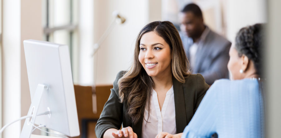 Woman looking at a computer smiling while another woman looks in