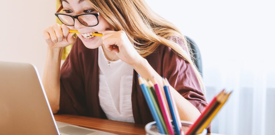 Woman looking stressed out and biting on a pencil while looking at her laptop screen