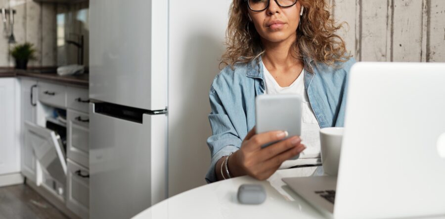 Woman looking at her phone while sitting at a table with a computer