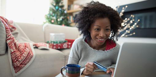 Woman sitting at table with coffee mug looking happy while looking at a computer. The room is decorated with Christmas stuff