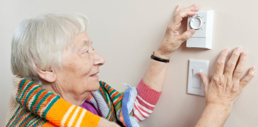 Older person in a blanket changing the temperature on her thermostat