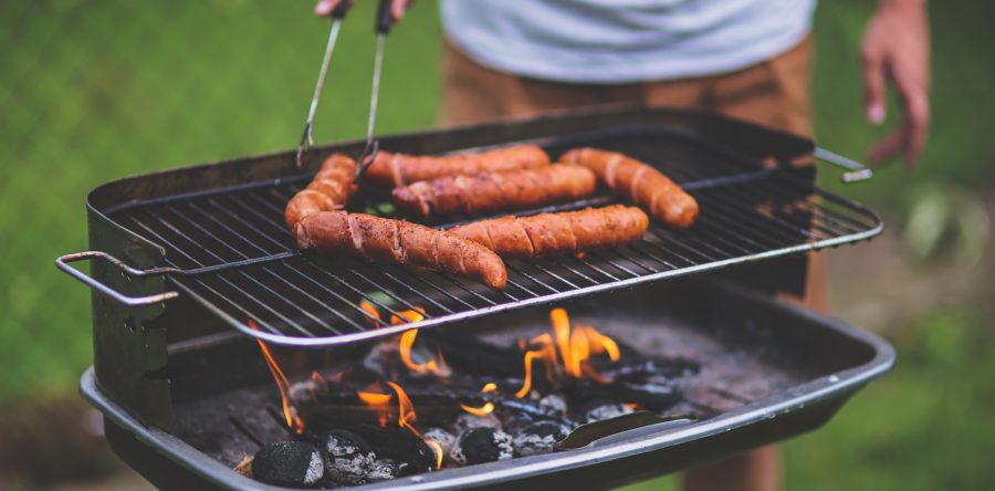 A man using tongs to grill hot dogs on a charcoal grill