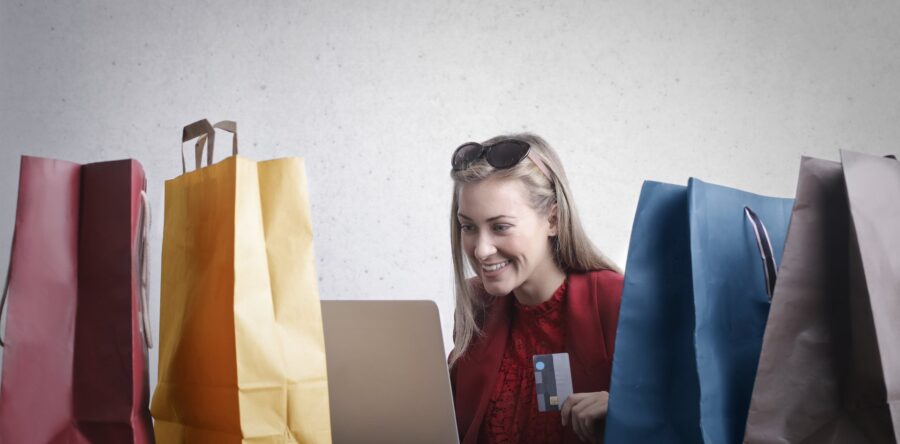 Happy woman surrounded by shopping bags with credit card in hand while looking at a laptop