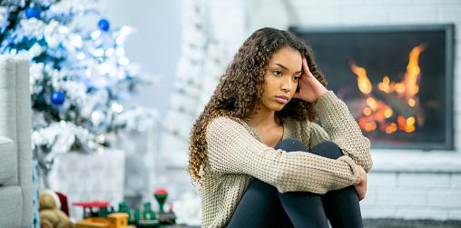 Girl sitting in Christmas Decorated room with fireplace lit behind her. She looks stressed