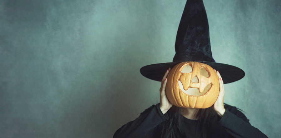 Person dressed up as a witch holding a jack-o-lantern in front of their face